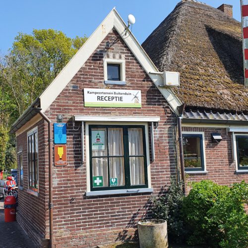 De receptie van Kampeerterrein Buitenduin in Schoorl is het kleine gebouwtje naast de stolpboerderij, vanaf de parkeerplaats aan de overkant van de weg.